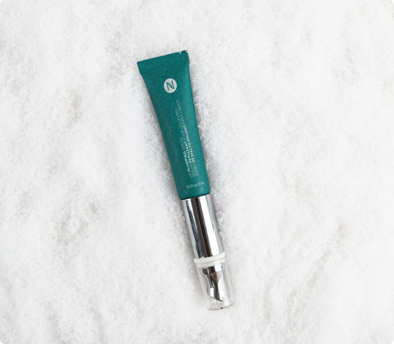 Neora’s hottest holiday limited-time must-have, Lip Plumping Serum, laying on a bed of snow.